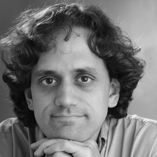 A dark haired man in a light colored shirt smiling at the camera, in black and white.